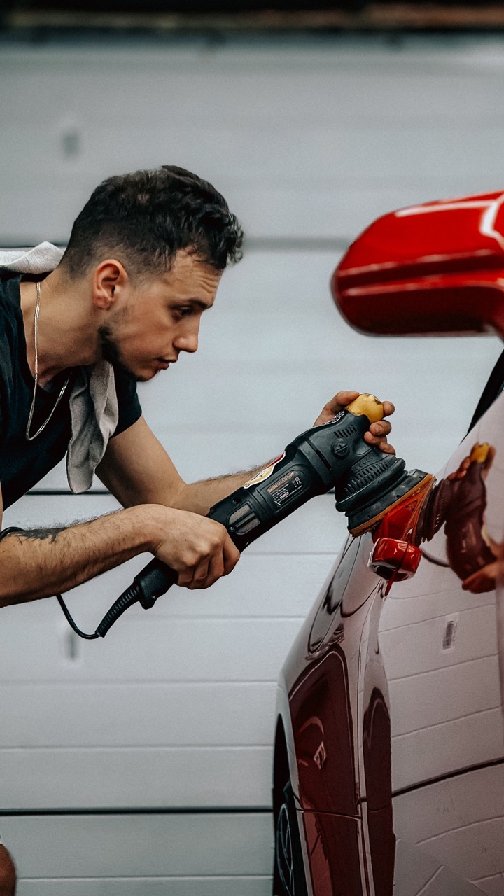 A detailer machine-polishing a car's paint by hand